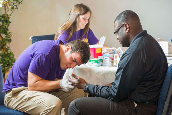 Undergraduate students Zeb Akers and Lauren Tredeau work the health screening desk at kCollege Hill Baptist Church. Being screened is church member Anthony McMullen.