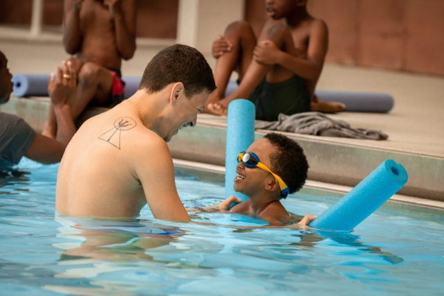 Swim instructor Victor Montano-Cruz works with child in pool.