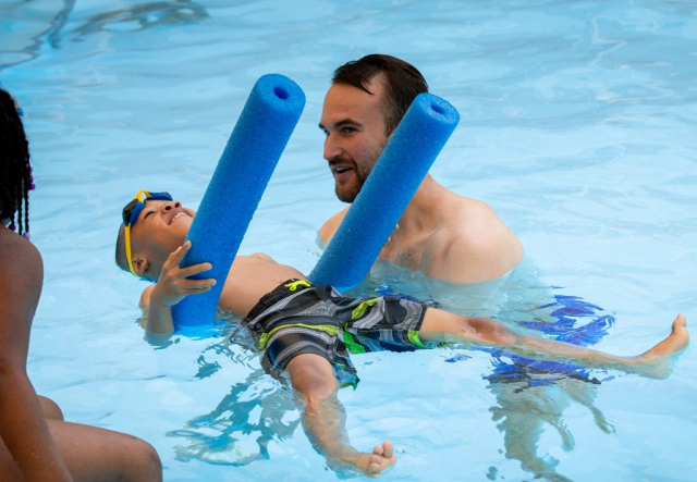Swim instructor Jake Peterson works with a child learning to float on the water.