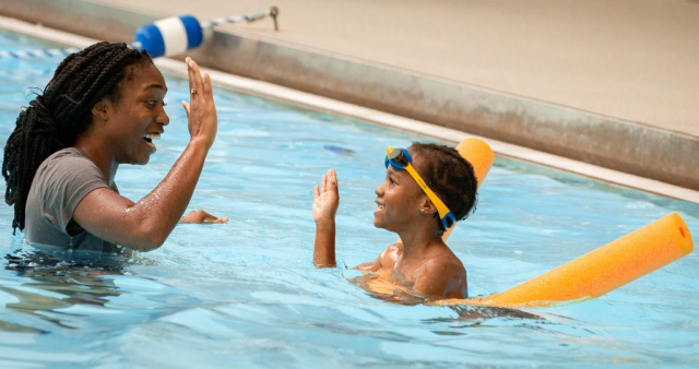 Swim instructor Kiara Williams and a child celebrate with a high five.